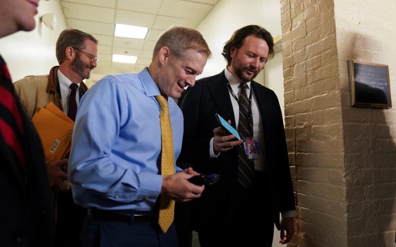 A man in a light blue shirt and yellow tie speaks into a phone being held up to him. 