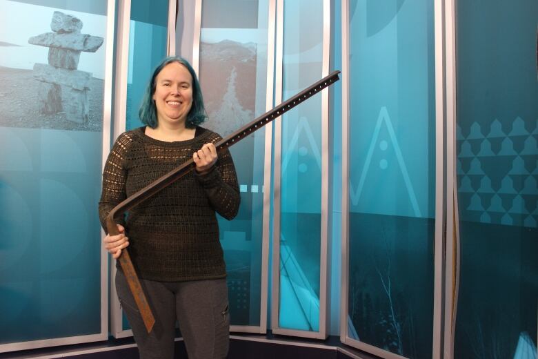 A woman with blue hair holds up a large angle iron that's bent at a 90 degree angle.