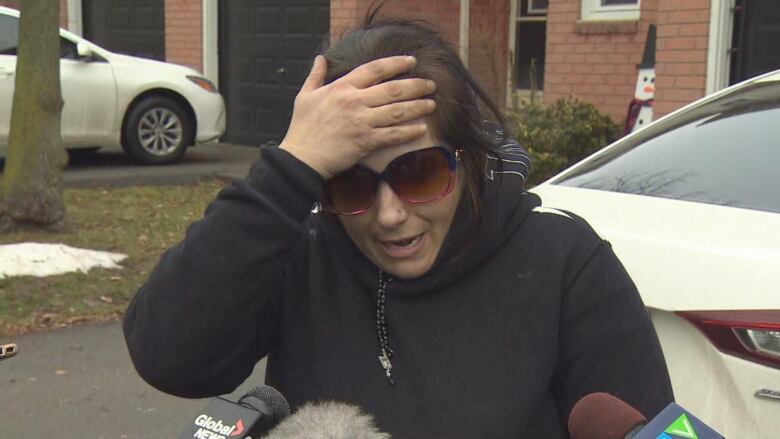 A distraught woman holds her forehead while talking with reporters. 