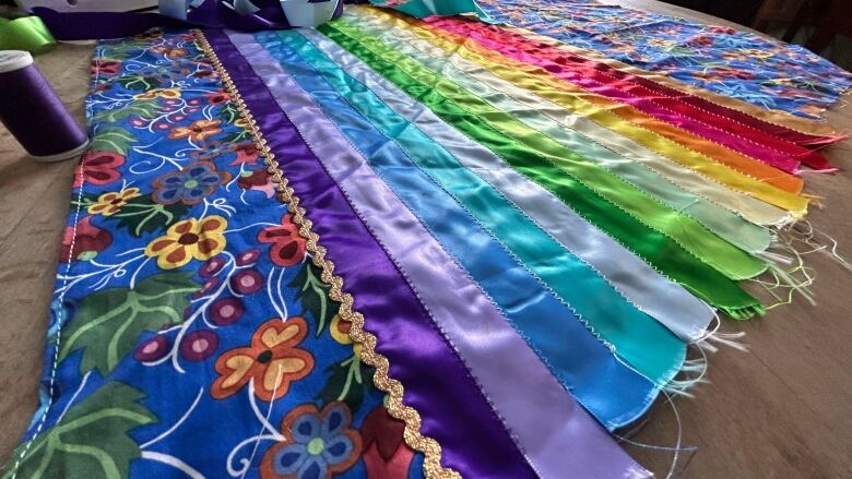 Colourful fabric and a rainbow of ribbons sewed into one panel lie on a flat surface.