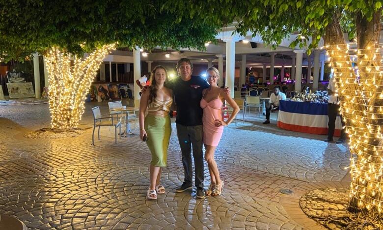 Two women and a man stand on a pebbled street.