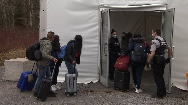 A white tent with glass doors and two police officers. Several young people with roller suitcases.