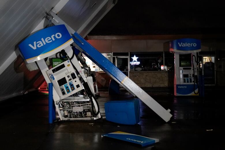 A gas station canopy lies toppled over near gas pumps.