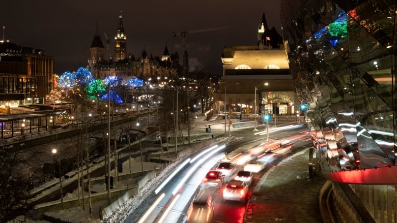 Vehicles in motion next to a downtown canal at night.