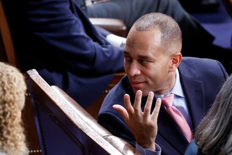 Man in a blue jacket and pink tie turns to speak with colleagues in the U.S. House chamber. 