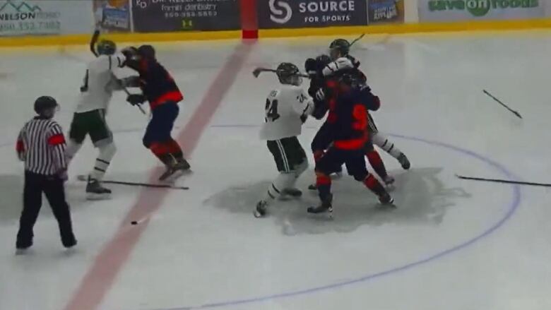 Several junior hockey players fight on the rink as a referee looks on.