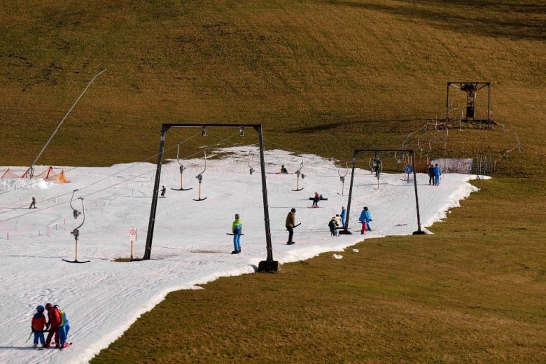 People near ski lift at a resort that has very little snow on the ground due to sparse snowfall and unseasonably warm weather in Europe during winter.