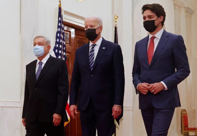 Three men wearing masks walk down a hallway together