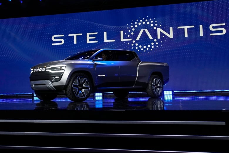 A blue pickup truck on a stage with the word Stellantis behind it.