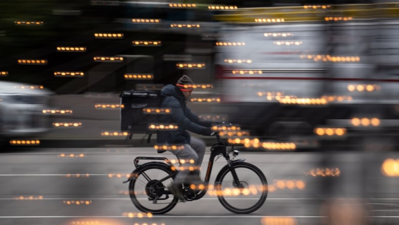 A man with a square-shaped backpack rides a bicycle.