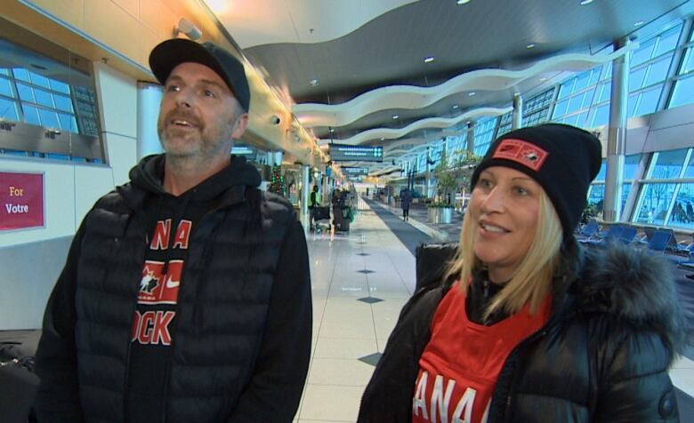 A man and a woman wearing black and red clothing stand inside an airport terminal.