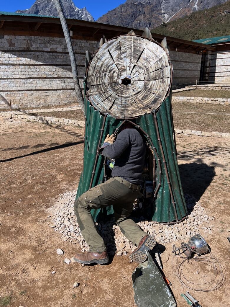 A man reaching inside a tree stump made of scrap metal.