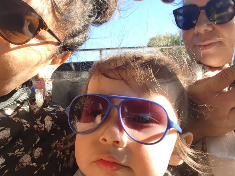 A woman, a child and another woman wearing sunglasses face the camera.