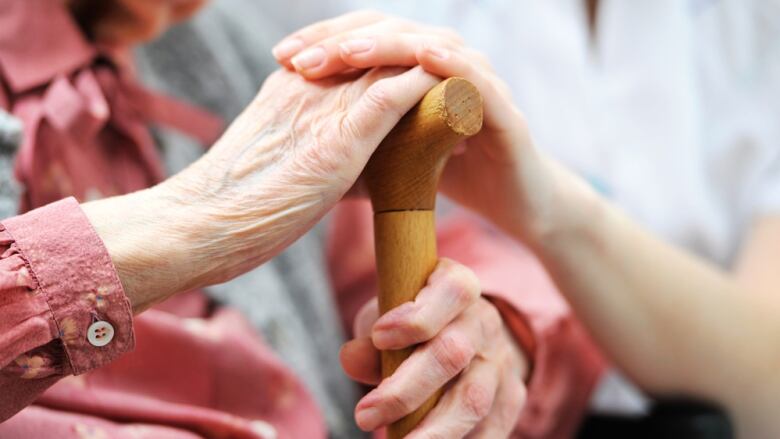 A caregiver places her hand on the hand of an elderly woman, who is holding a cane. 