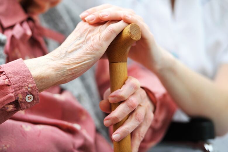 A caregiver places her hand on the hand of an elderly woman, who is holding a cane. 