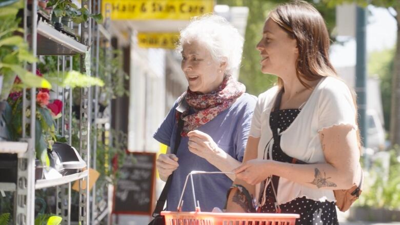 A woman accompanies an elderly woman to shop for plants. 