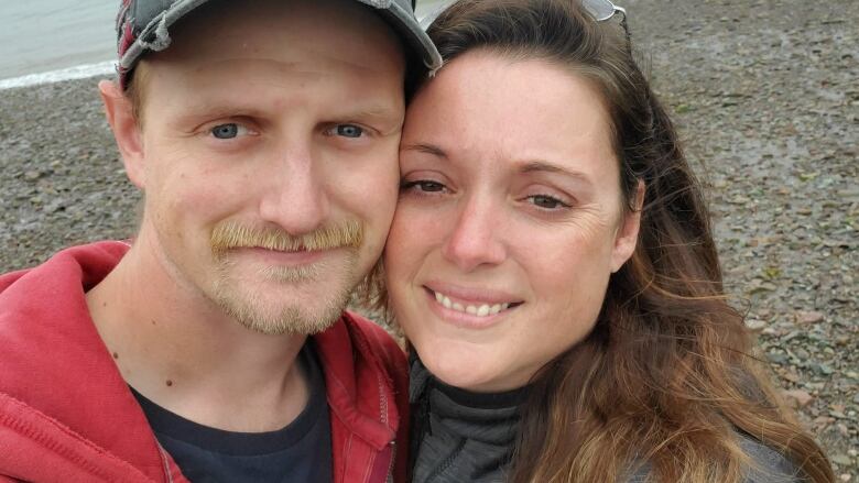 A man and woman smile at the camera on a beach.