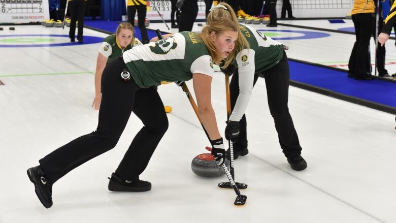 Two curlers sweep a stone that was delivered by another player.