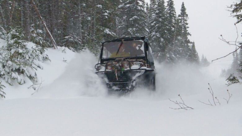 Snow flicks from the side tracks of an amphibious vehicle as it descends a snow-covered mountain.