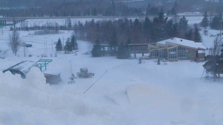 Looking down the mountain toward the ski chalet, there are snowmaking guns and a groomer shown in this panoramic image.