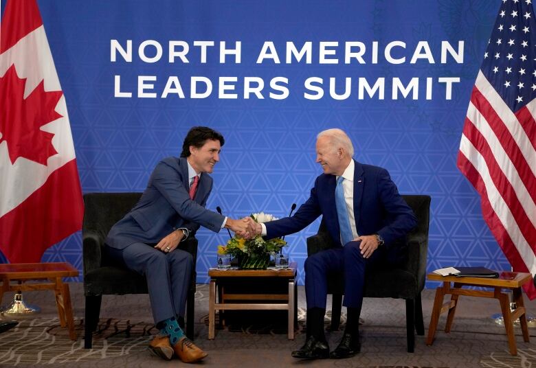 Justin Trudeau and Joe Biden smile and shake hands while seated at chairs.