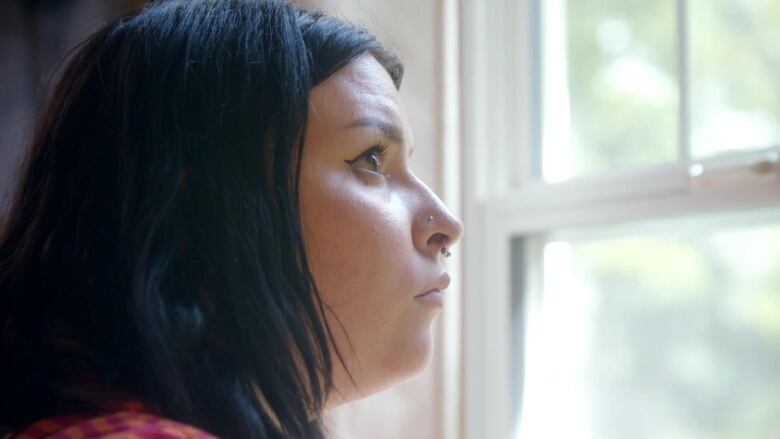 A closeup of a woman with dark hair staring out a window, with a contemplative look on her face.