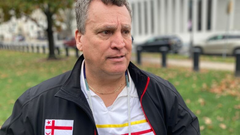 A man wearing a dark windbreaker that says Mi'kmaq First Nation stands in front of the legislature.