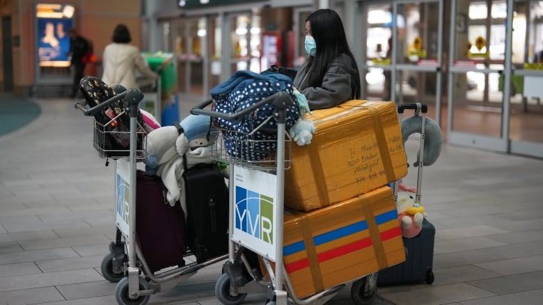 A woman stands with a luggage cart that says YVR on it outside the Vancouver airport.