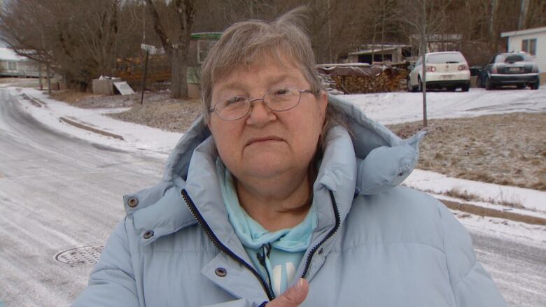 A woman seen from shoulders up looking right into the camera. She's wearing a baby blue jacket and hoodie, as well as circular glasses. 