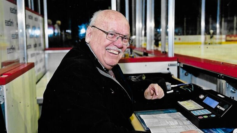 A man is seated at the side of an ice rink.