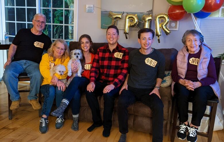 A group sits on a living room rouch, with The Price is Right balloons in the background.