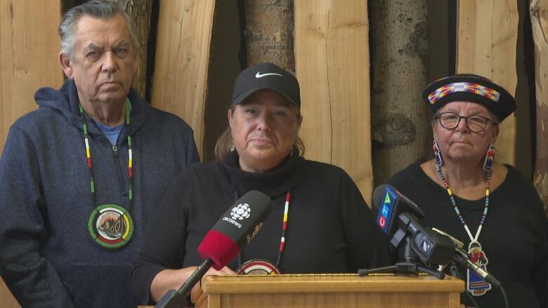 A man and two women stand in front of a wooden background.