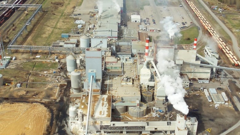 An overhead shot of a pulp mill, with smoke spewing from stacks and various buildings visible.