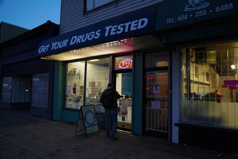 The words Get Your Drugs Tested are seen on an awning over a storefront on East Hastings Street. A customer walks through the door below an open sign.