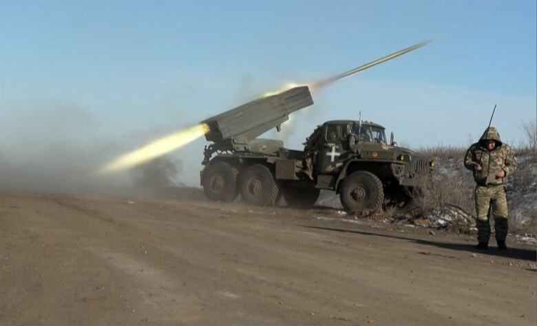 A soldier looks away as a rocket is fired from a mobile launcher.