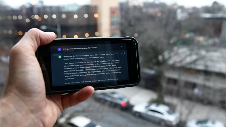 A hand holds a smart phone on which the AI text generator answers a prompt. The text is too small to read. 