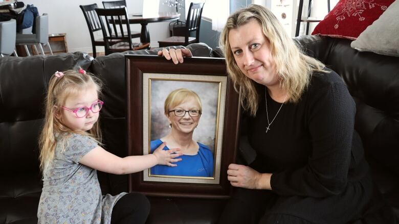 A woman and her daughter hold a portrait of a woman who died after waiting roughly seven hours for treatment at a Cape Breton hospital. 