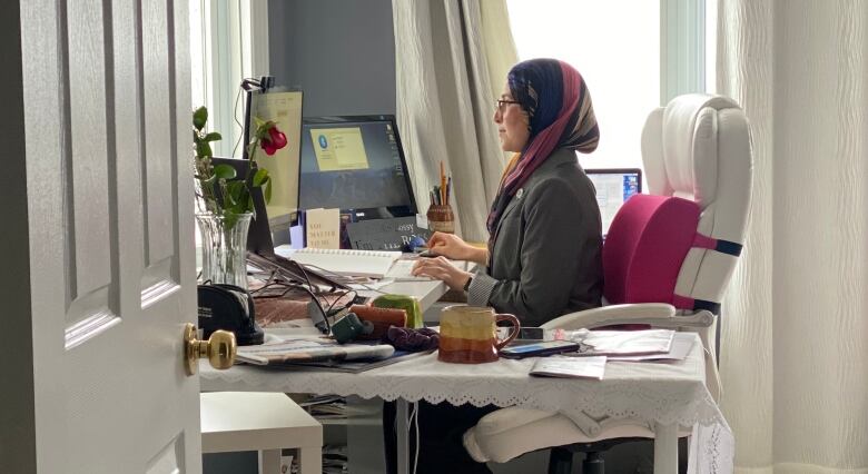 A woman sits at her desk looking at a computer.