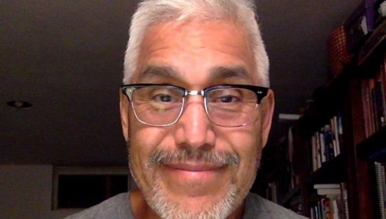 An Indigenous man, in a grey t-shirt and wearing glasses, smiles for a profile photograph. 