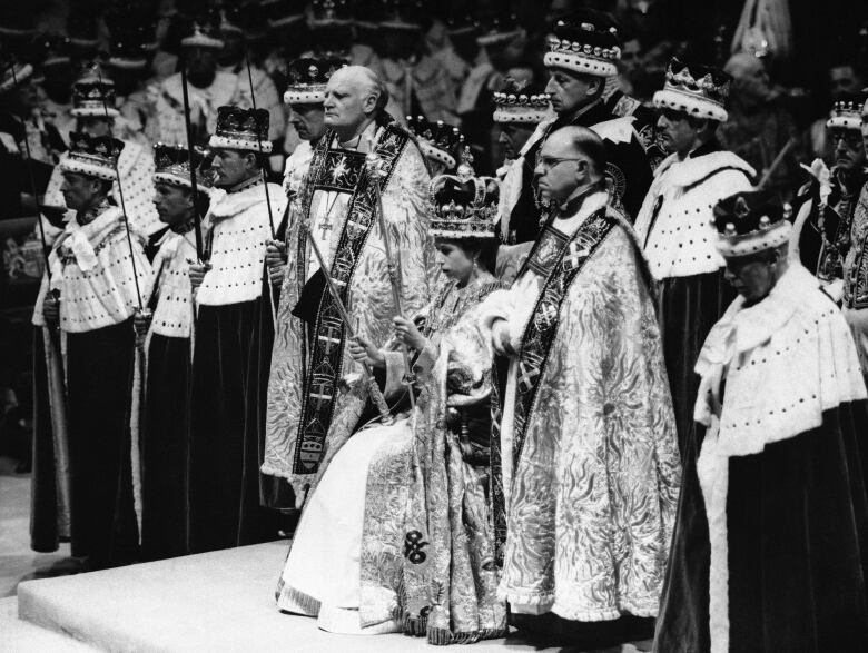 Several people stand around a seated person with a crown on their head.