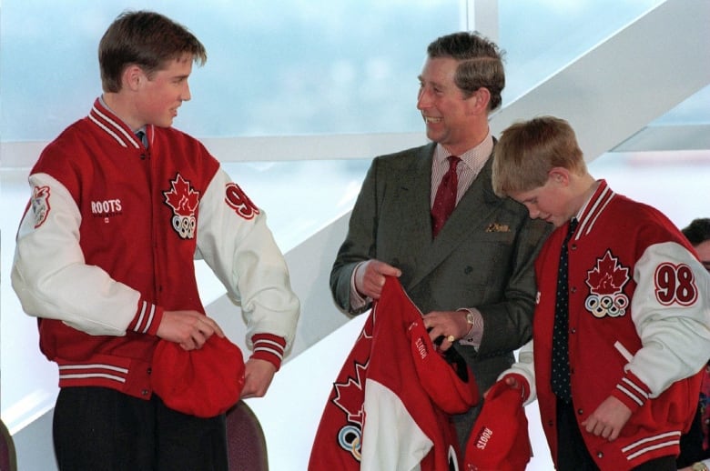 Three people stand laughing while holding hats and a jacket.