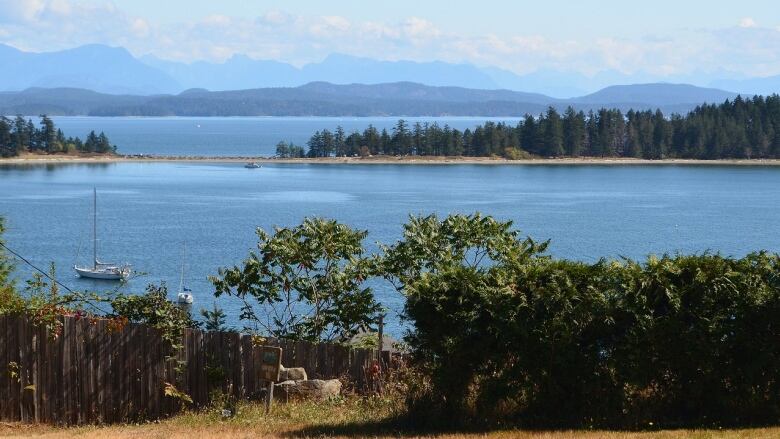 A beautiful view looking out from the We Wai Kai campground on Quadra Island, with trees, ocean and layers of mountains in the background.