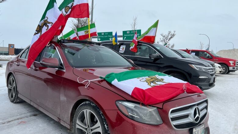 A row of vehicles are pictured lined up on a parking lot. Each are decorated with Iranian flags.