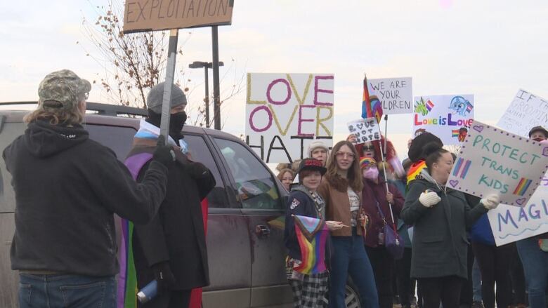 a group of about a dozen people stand beside a vehicle and hold signs that read messages like 