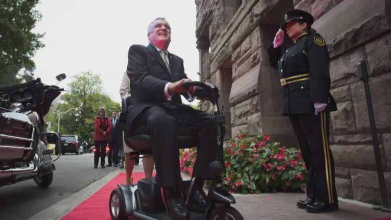 A man on a motorized scooter can be seen with a person saluting next to him.