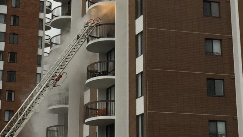 A fire can be seen in one apartment of a large apartment building complex. A long ladder leads up to the window. 