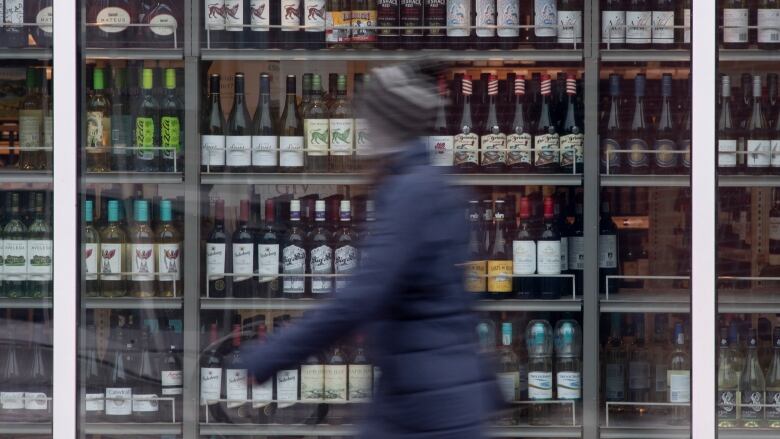 A person walks past shelves of bottles of alcohol on display.