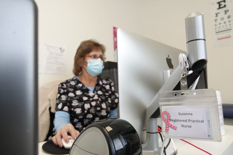 A woman in medical scrubs covered in teacups and wearing a face mask works at a computer.