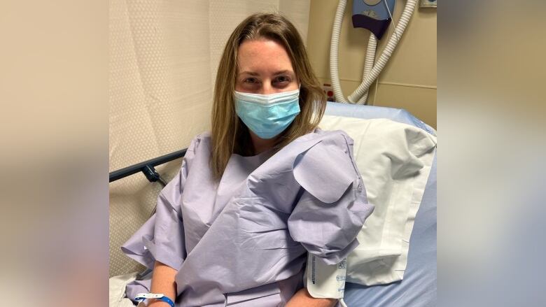 A woman with mask sits on a hospital bed.