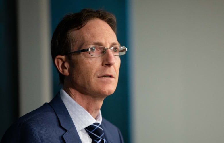 A man wearing a blue suit and glasses speaks at a podium.